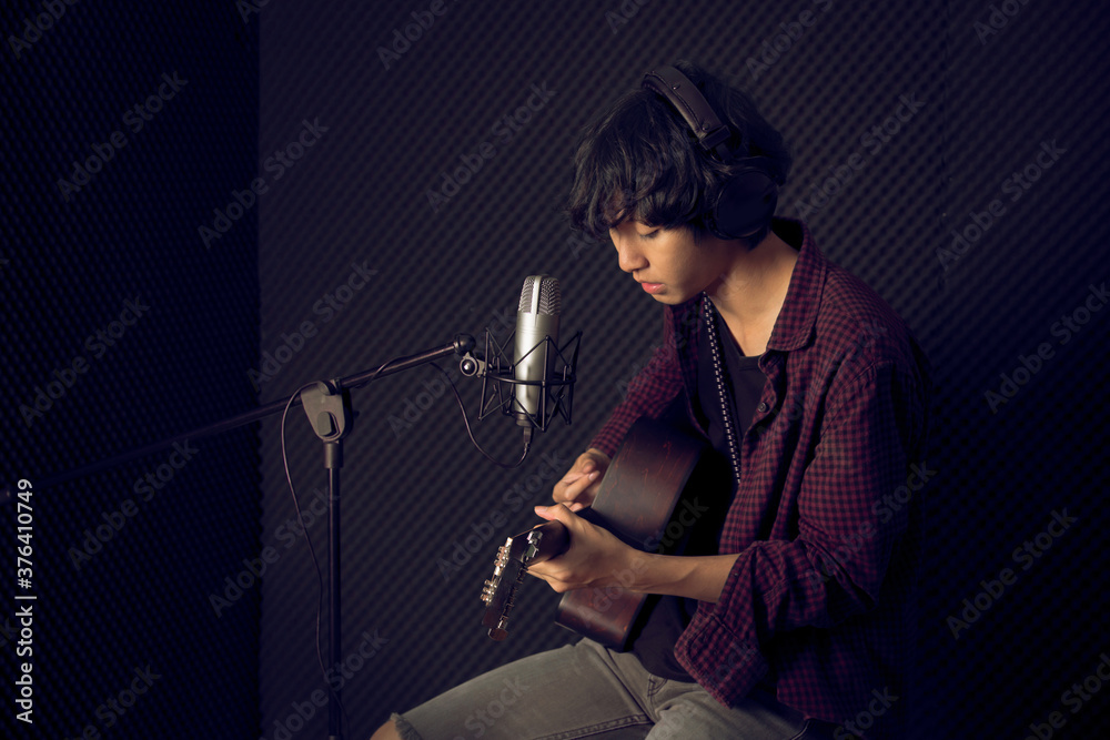 Young asian man plaing guitar in front of microphone in music studio record room Young asian man plaing guitar in front of microphone in music studio record room