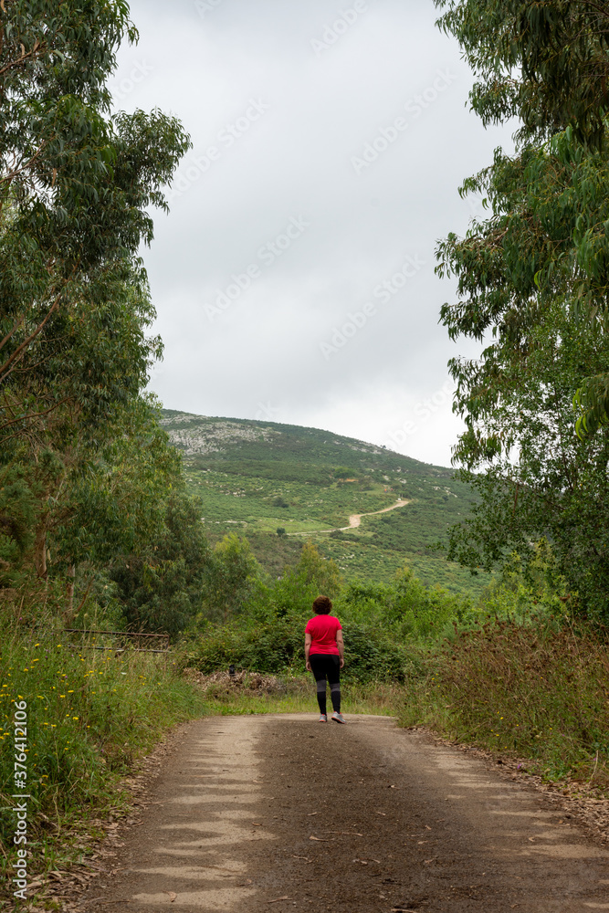General shot of adult woman with sports clothes, walking along a forest path, among eucalyptus trees, on a cloudy morning, in Cantabria, Spain, in portrait