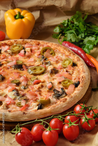 Mexican pizza on the table with cherry tomatoes and bell peppers, hot peppers and herbs.