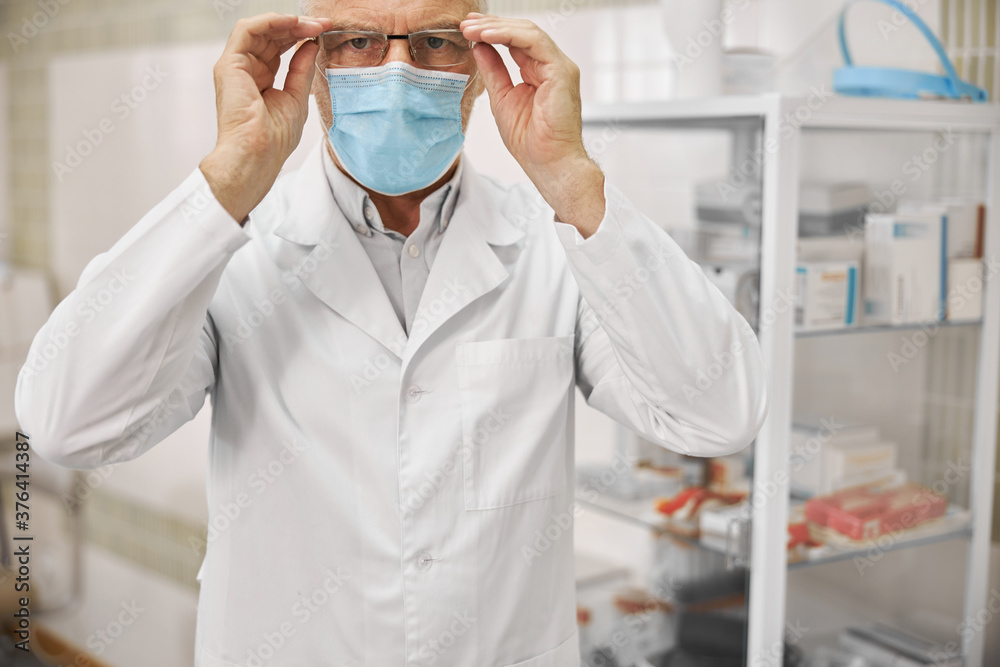 Naklejka premium Serious healthcare worker in a labcoat putting glasses on