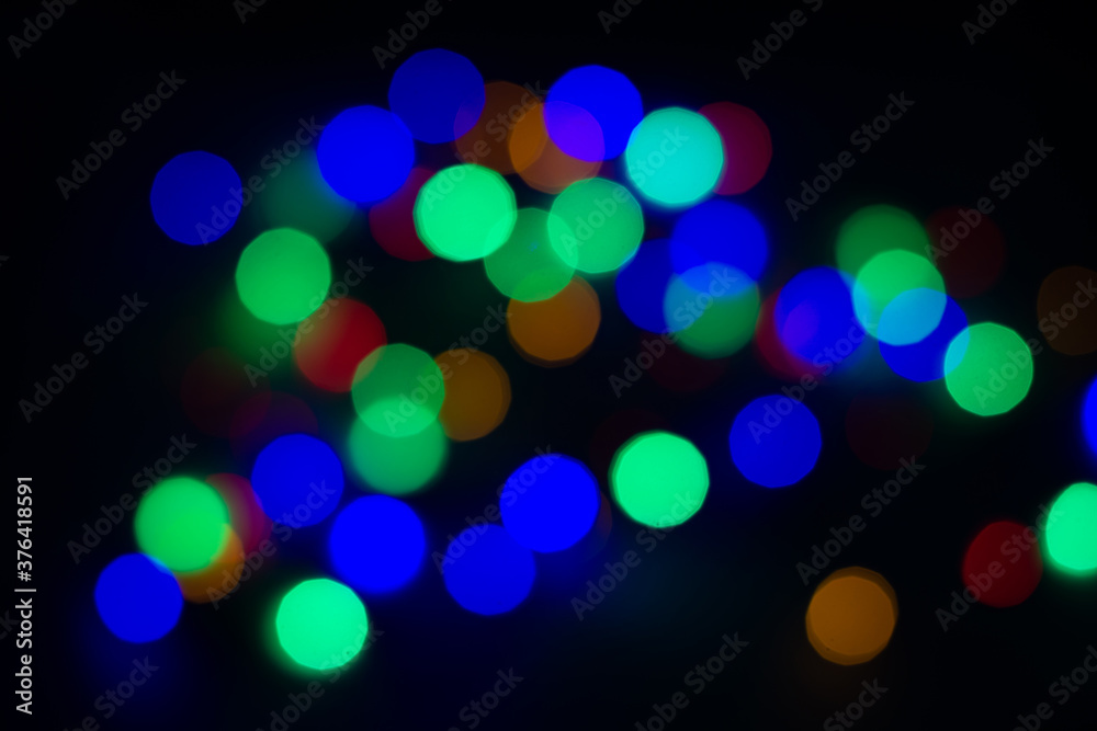 Blurry colored circles on a black background. Blurred garland on a black background, christmas background.