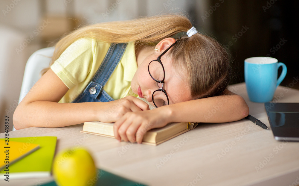 Tired school girl sleeping at table with book Tired school girl sleeping at table with book