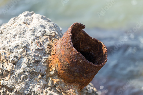 A piece of truncated, broken off rusty pipe sticks out of a piece of concrete. Metal rust is a broken construction. A piece of Rusty pipe on the sea-line. Building debris thrown ashore