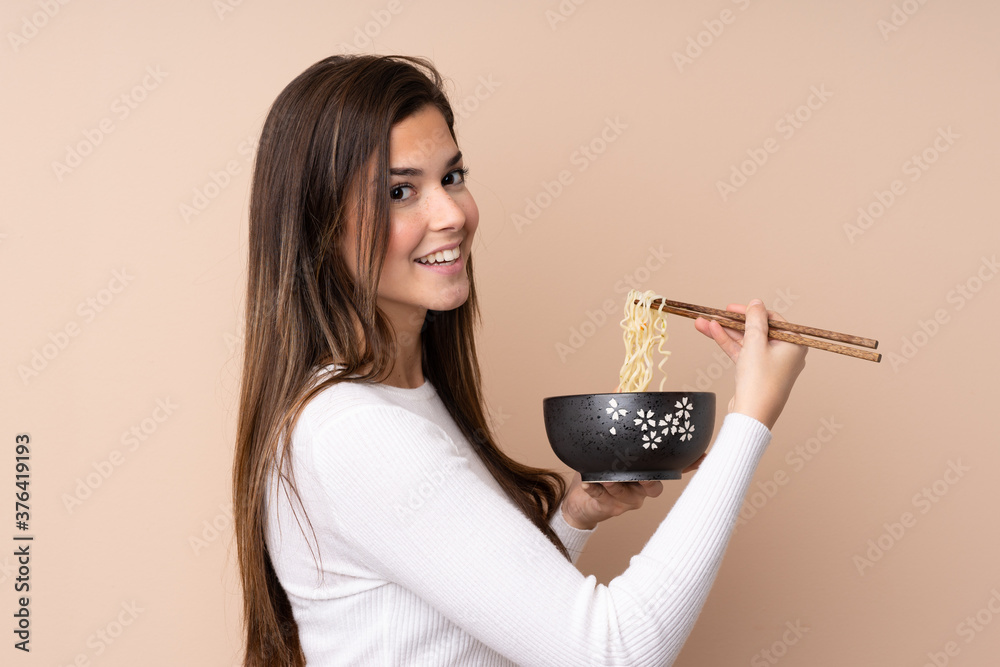 Teenager girl over isolated background holding a bowl of noodles with chopsticks Teenager girl over isolated background holding a bowl of noodles with chopsticks