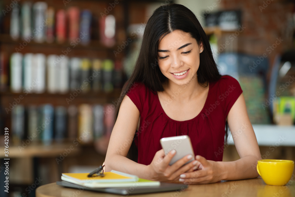 Smiling Asian Woman Texting On Smartphone While Having Coffee Break In Cafe Smiling Asian Woman Texting On Smartphone While Having Coffee Break In Cafe