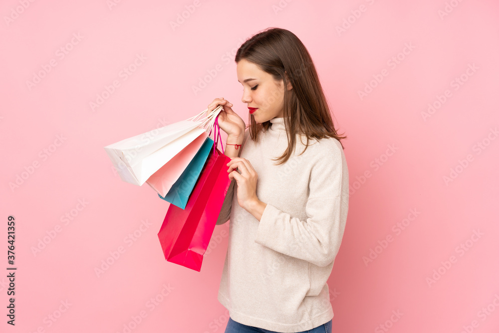 Teenager girl isolated on pink background holding shopping bags