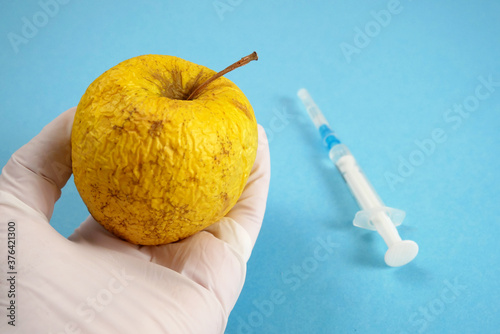 apple in genetic engineering laboratory with syringe and test tubes on blue background, gmo food concept
