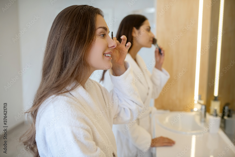Two young women doing make up near the mirror Two young women doing make up near the mirror