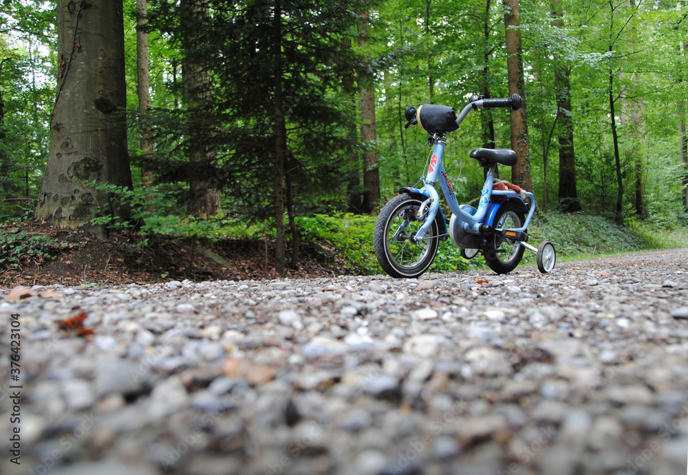 Hellblaues kinderfahrrad mit stutzräder auf kiesweg im wald