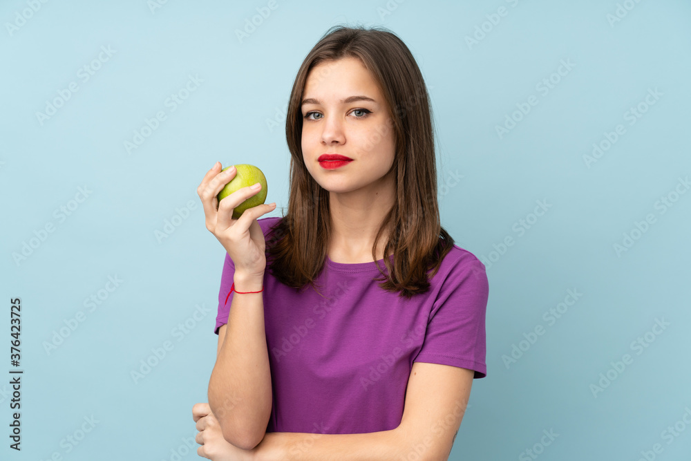 Teenager girl isolated on blue background with an apple Teenager girl isolated on blue background with an apple