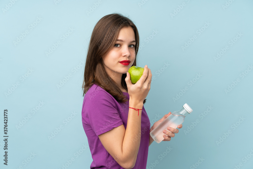 Teenager girl isolated on blue background with an apple and with a bottle of water Teenager girl isolated on blue background with an apple and with a bottle of water