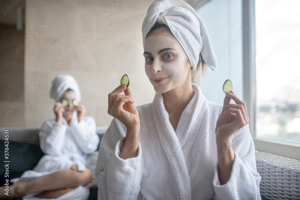 Young woman with towel on her head holding cucumber slices Young woman with towel on her head holding cucumber slices