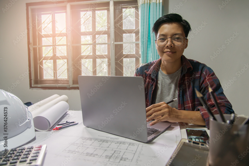 Concept people, smiling Asian engineer on the desk with a blueprint in the home office, Sunset light.Selective Focus Concept people, smiling Asian engineer on the desk with a blueprint in the home office, Sunset light.Selective Focus
