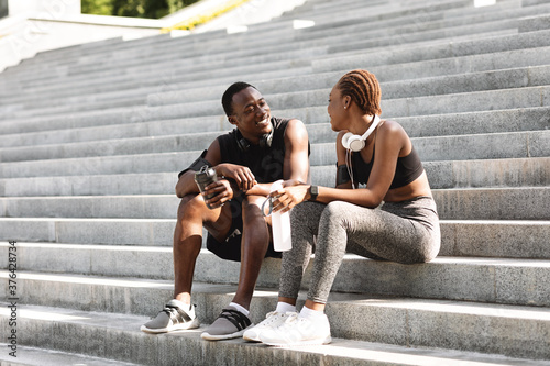 Positive African Couple Resting After Fitness Workout Outdoors, Sitting On Urban Steps