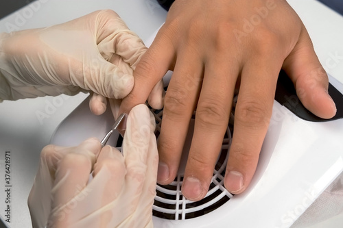 Woman manicurist master is pushing cuticle on man's finger using pusher, closeup hands. Professional manicure in beauty salon. Hygiene and care for hands. Beauty industry concept.