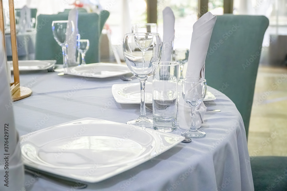 The table in the restaurant is served for lunch. On a table with a white tablecloth, empty wine glasses, a plate, napkins. Selective focus The table in the restaurant is served for lunch. On a table with a white tablecloth, empty wine glasses, a plate, napkins. Selective focus