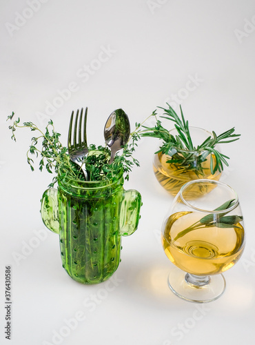 Rosemary herbal tea in glass cups, spoon and fork in bottle with thyme on white background, vertical image with copy space