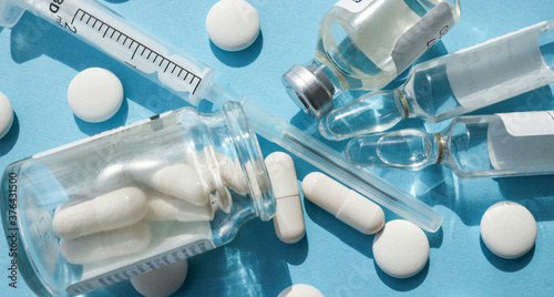 white capsules, close-up. near the capsules there is a needle, a syringe, a glass jar with white tablets and ampoules. on a blue background. banner photo