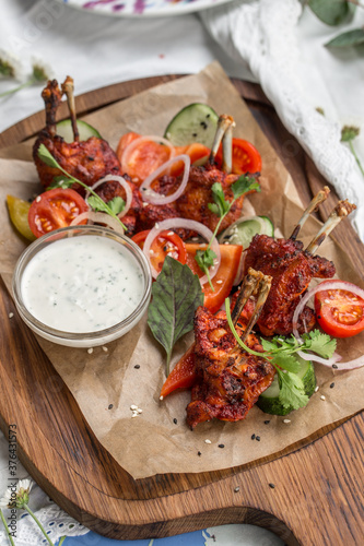 roasted chicken wings with paprika, white sauce and vegetables on wooden board on the table