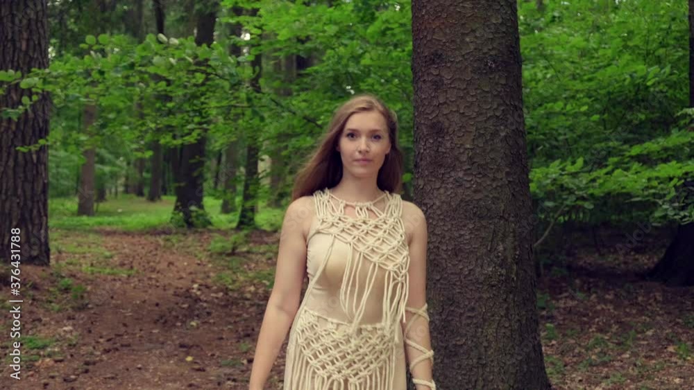 A beautiful young blonde woman looks at the camera and goes to a meeting. Against the background of a dense forest. 4K video.