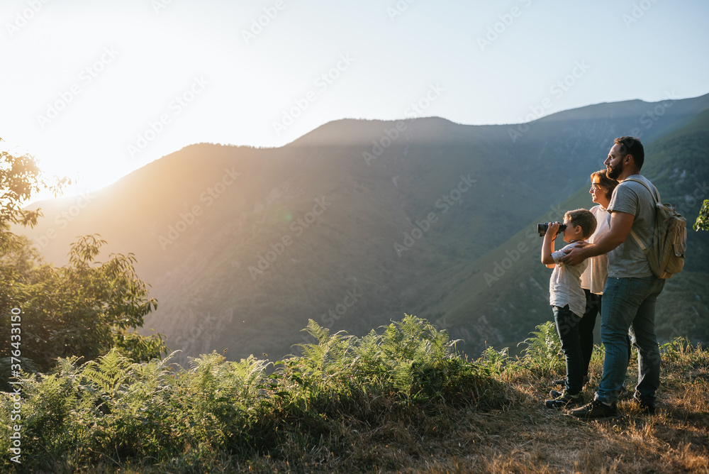 father, wife and son with a six year old boy looking through binoculars on the mountain at sunset