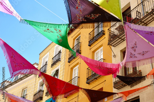 Multicolored Spanish shawls are strung between the balconies outside on the street. The decorated ambient creates a festive mood. La Latina district, Madrid, Spain