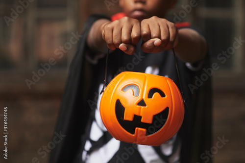 Unrecognizable boy wearing modern Halloween costume demonstrating plastic Jack O' Lantern basket for candies while trick-or-treating photo