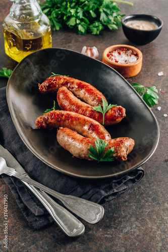 Grilled sausage with greens on black plate over dark background.