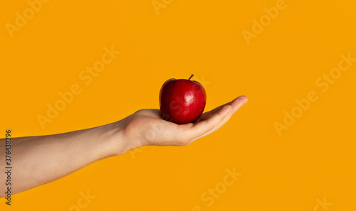 Closeup of young guy holding ripe red apple over orange background