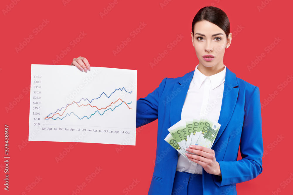 Business woman in blue suit holding money, cash, euro banknotes and paper graph with diagram isolated on red background Business woman in blue suit holding money, cash, euro banknotes and paper graph with diagram isolated on red background