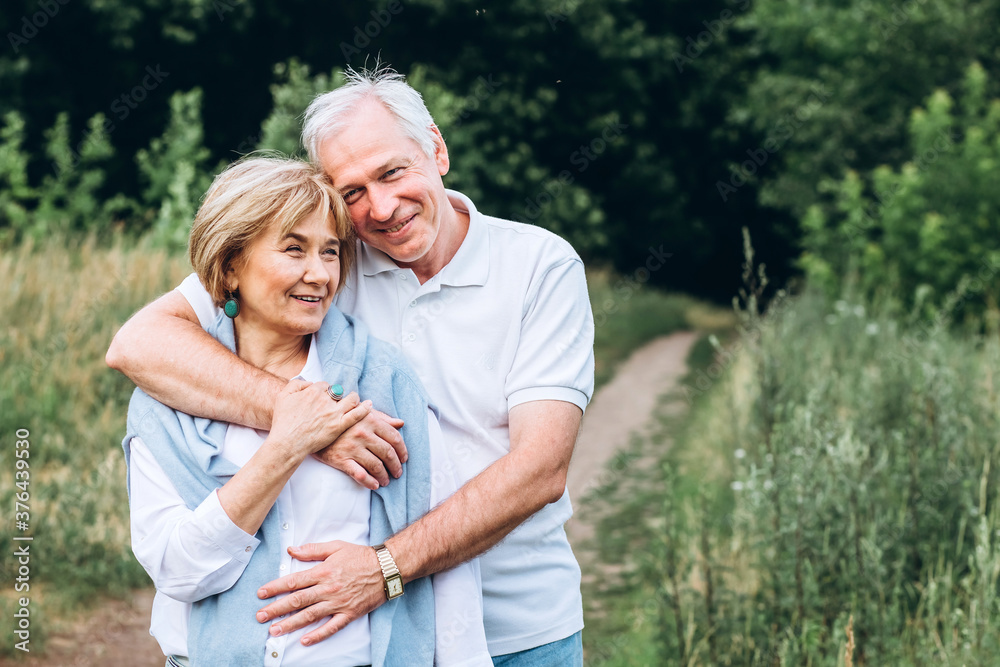 mature couple is walking with dog in park. Elderly couple resting in nature with a dog. Full-length portrait of an elderly man and woman in white shirts and jeans. Stylish and modern grandparents.