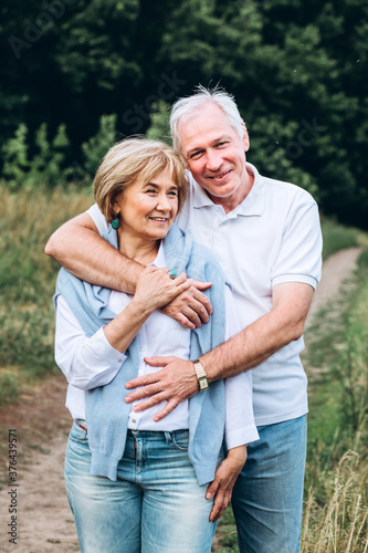 mature couple is walking with dog in park. Elderly couple resting in nature with a dog. Full-length portrait of an elderly man and woman in white shirts and jeans. Stylish and modern grandparents.