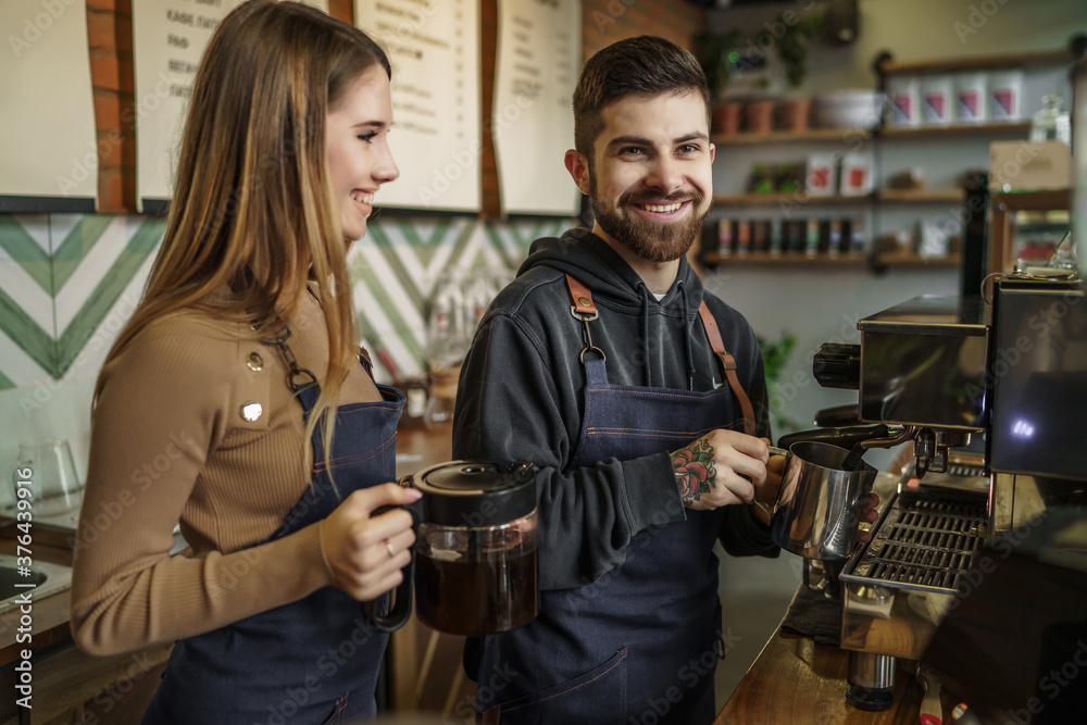 Two young smiling and pretty barista at work. Professional barista team brewing coffee using coffee machine in coffee shop Two young smiling and pretty barista at work. Professional barista team brewing coffee using coffee machine in coffee shop