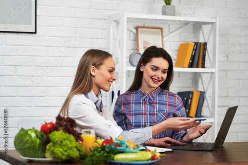 A smiling nutritionist advises a young patient woman on proper nutrition and dieting. Diet based on vegetables and fruits