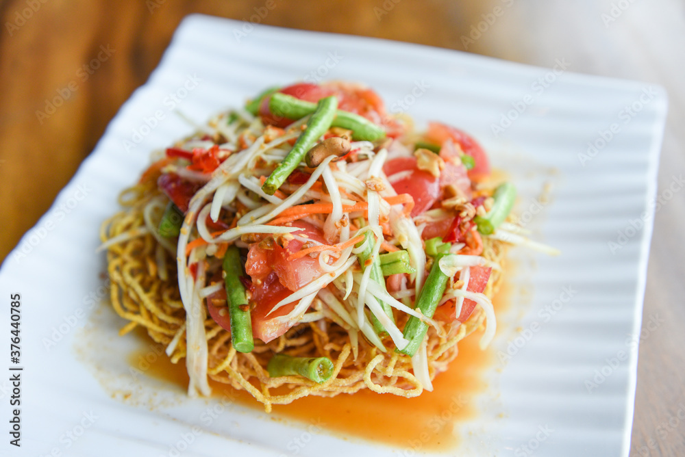 Papaya salad spicy on crispy noodles on white plate , Thai food with yardlong bean herbs and spices ingredients chilli tomato garlic / Papaya salad spicy on crispy noodles on white plate , Thai food with yardlong bean herbs and spices ingredients chilli tomato garlic /