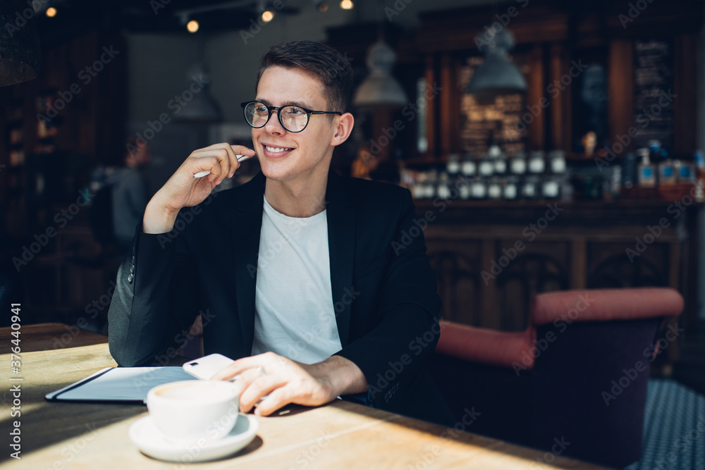 Positive cafe manager sitting with smartphone and cup of coffee