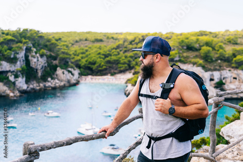 A tourist man with a backpack enjoys the views of a cove Macarella beach