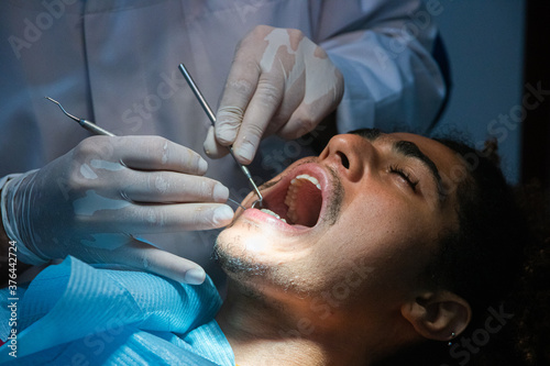 Odontologia avanzada, cuidados confiables. Joven paciente afro-americano en una clinica dentista realizando una limpieza bucal . Dentista examinando los dientes del paciente en una clinica profesional photo