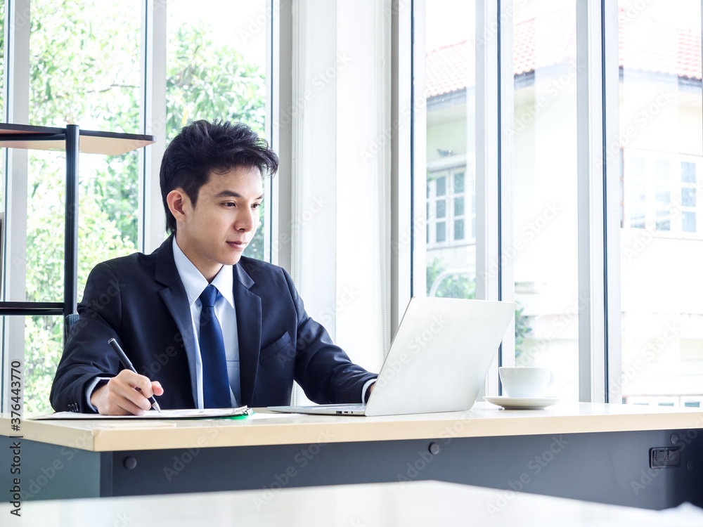 Young Asian businessman in suit working with laptop computer in office.