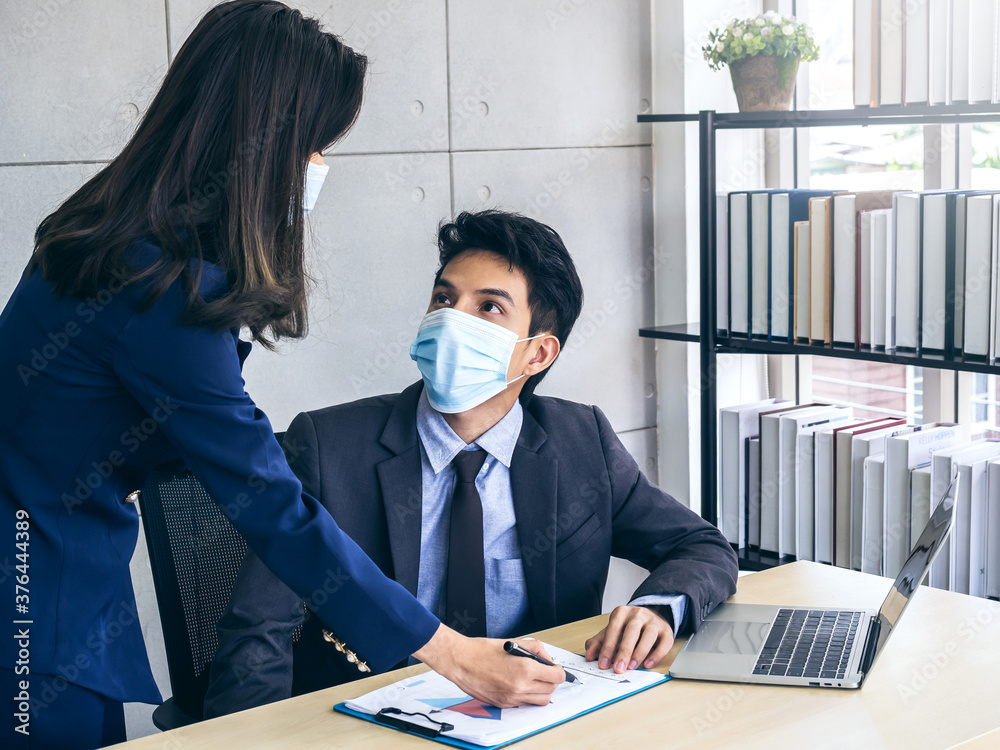 Asian business man and woman wearing suit and protective face masks using computer on desk, meeting and working together in office. Asian business man and woman wearing suit and protective face masks using computer on desk, meeting and working together in office.