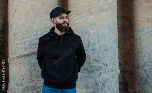 City portrait of handsome hipster guy with beard wearing black blank hoodie or sweatshirt with space for your logo or design. Mockup for print