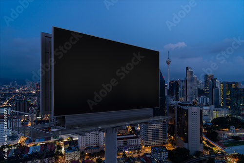 Blank black road billboard with KL cityscape background at night time. Street advertising poster, mock up, 3D rendering. Side view. The concept of marketing communication to promote or sell idea.