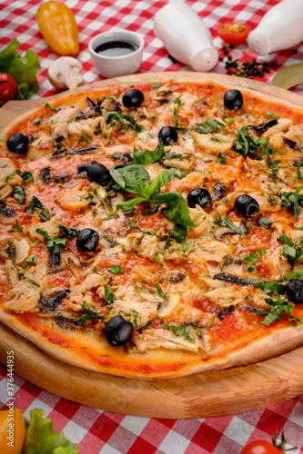 Rustic pizza with chicken meat, cheese, tomato, olive, mushrooms and tomatoes sauce, served on a wooden board for a dinner in italian restaurant background, top view. Classic Italy food. Close up
