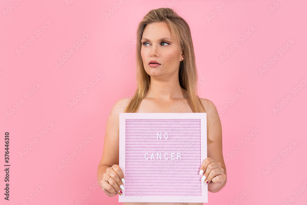 Young blonde woman hold board with inscription no cancer on pink background. Breast cancer awareness. Young blonde woman hold board with inscription no cancer on pink background. Breast cancer awareness.
