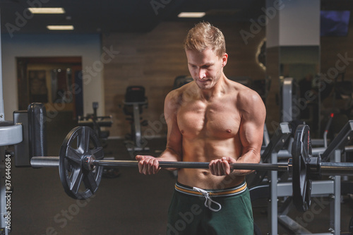 Muscular man working out in gym doing exercises with barbell at biceps, beginner male