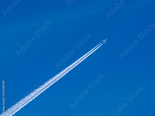 White jet passenger plane flying at high altitude in a blue clear cloudless sky. Behind the aircraft is a white condensation trail of water vapor.