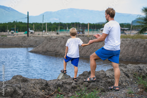 Father and son walk along man made breeding fish lake mountain background. Happy childhood. Home natural child education, fathers day, dad responsibilities, influence on son worldview formation