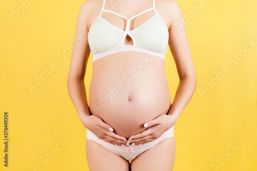 Close up of pregnant belly at yellow background. Mother is wearing colorful underwear and holding her abdomen. Parenthood concept. Copy space