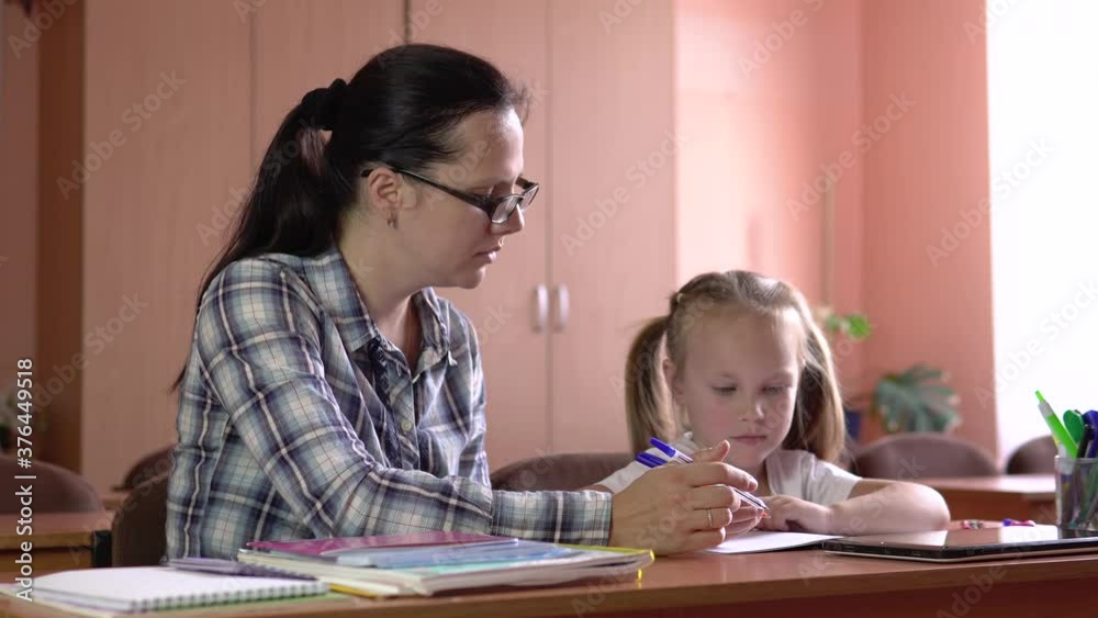 Little beautiful girl is studies with the teacher in the school class. Draws in a notebook with a pen. Preschool education.4k Little beautiful girl is studies with the teacher in the school class. Draws in a notebook with a pen. Preschool education.4k