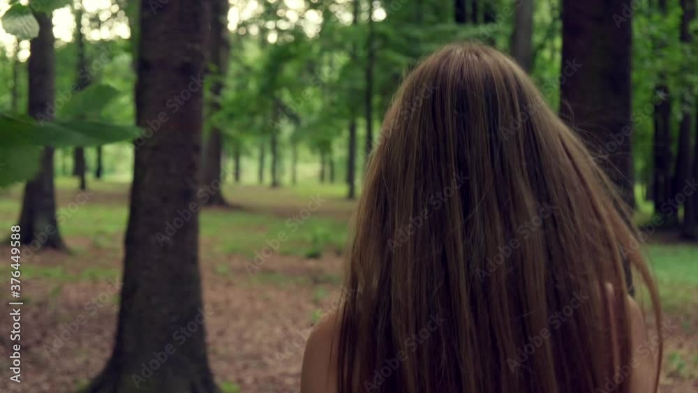 A view from the back on a young beautiful blonde girl with long hair. The girl walks through the forest in summer. 4K video. A view from the back on a young beautiful blonde girl with long hair. The girl walks through the forest in summer. 4K video.